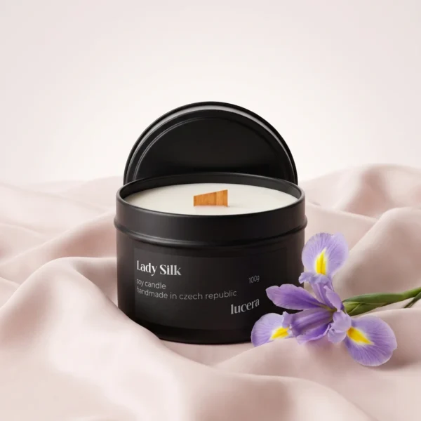Svíčka Lucera Lady Silk v černé plechovce na světle růžovém hedvábí vedle květu kosatce
