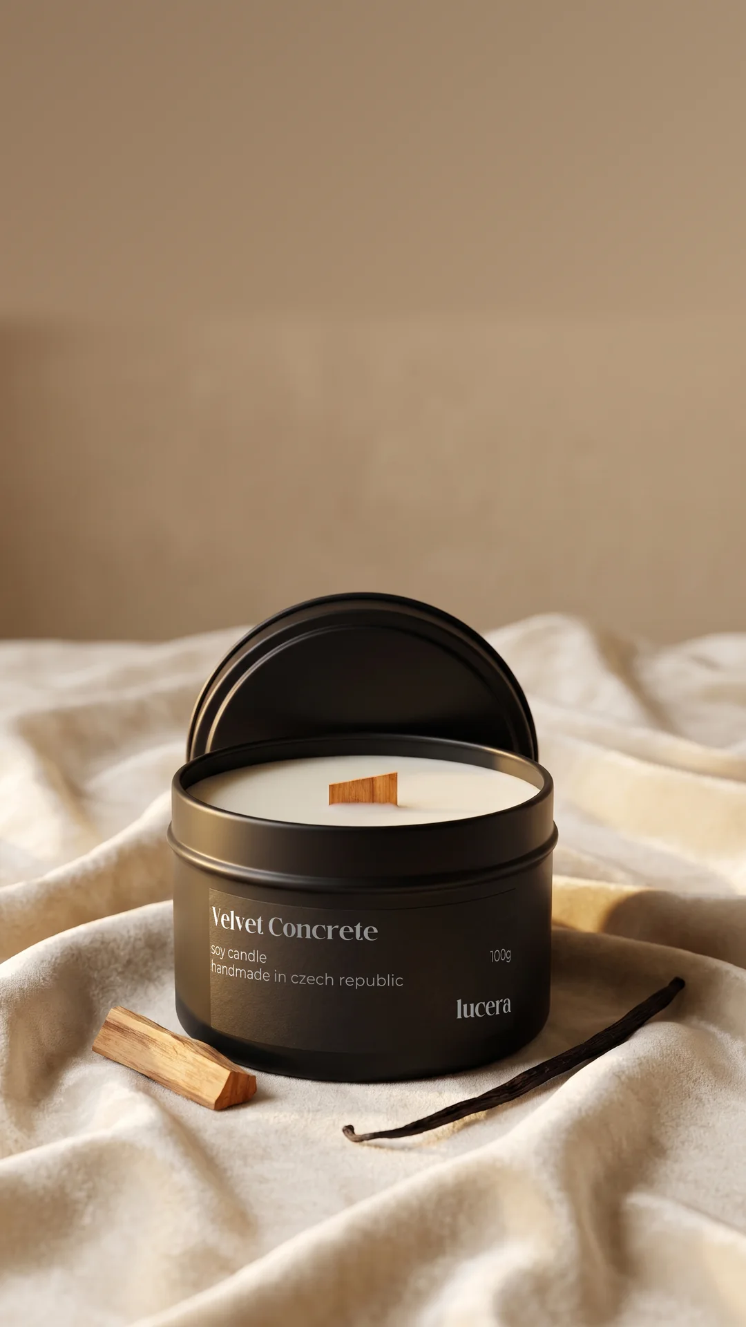 Svíčka Lucera Velvet Concrete v černé plechovce na krémové látce vedle dřívka palo santo a vanilkového lusku