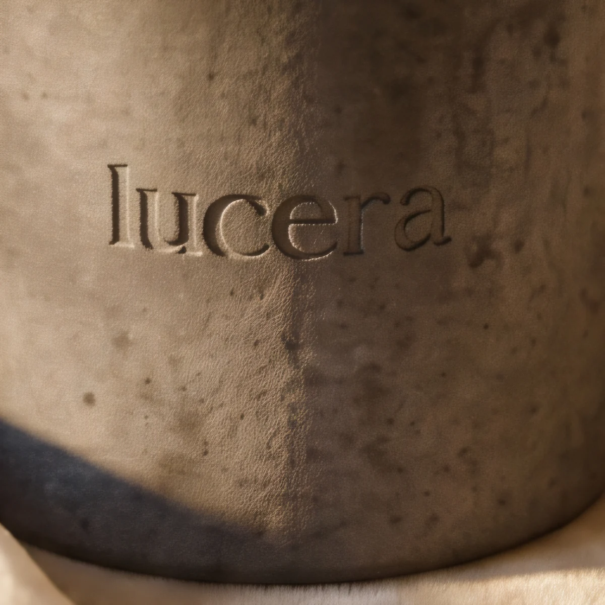 Detail embosovaného loga lucera v šedém betonu svíčky Velvet Concrete